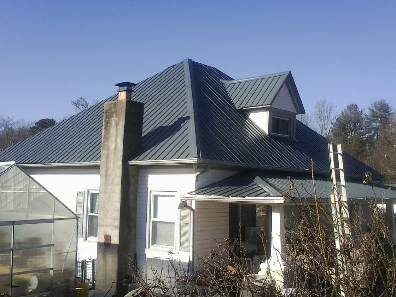 Dark blue standing seam metal roof on a white farmhouse with dormer — Slate & Tile Roof Repair by Roofing Brothers in Greenville